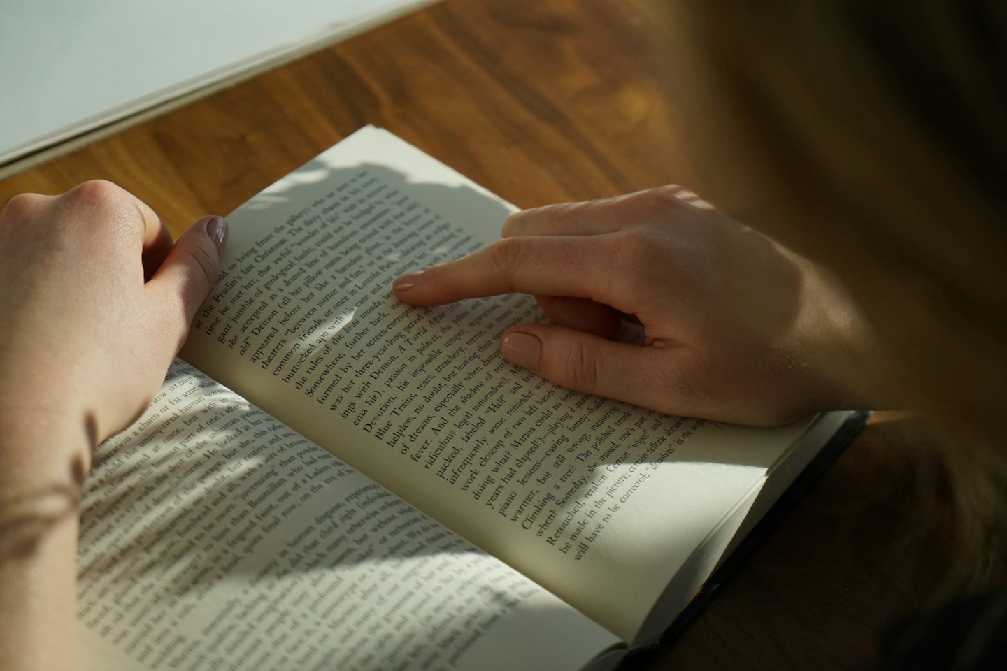 Hands holding an open book with a finger pointing to text.